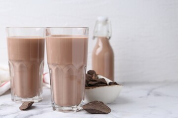 Tasty chocolate milk in glasses and pieces of chocolate on white marble table, closeup. Space for text