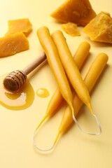 Beautiful beeswax candles, dipper with honey and pieces of wax on beige background, closeup