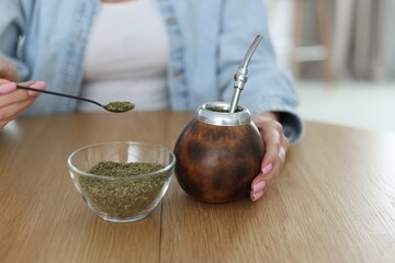 Woman making traditional yerba mate tea at wooden table indoors, closeup