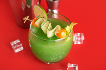 Glass of green bloody mary cocktail garnished with physalis berries and cucumber slice on red...