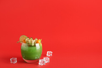 Glass of green bloody mary cocktail garnished with physalis berries and cucumber slice on red...
