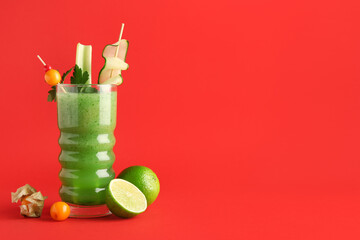 Glass of green bloody mary cocktail garnished with berries, celery and cucumber slice on red...