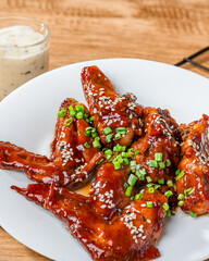 A plate of chicken wings with sesame seeds and green onions. The plate is on a wooden table