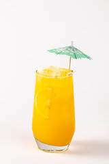 A glass of orange juice with a green umbrella on top. The umbrella is made of paper and is placed over the glass