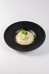 A black bowl with a white substance in it and a green leaf on top. The bowl is placed on a white background