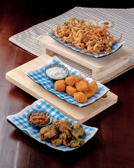 Three plates of food are displayed on a wooden board. The plates contain different types of food, including fried chicken, broccoli, and onion rings. The presentation is colorful and appetizing