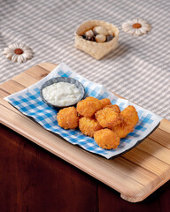 A plate of fried food with a blue and white checkered napkin. The food is covered in a light sauce and is served on a wooden board
