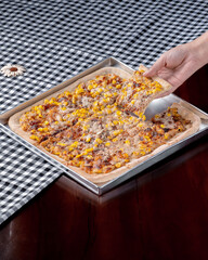 A person is holding a slice of corn pizza. The pizza is cut into four pieces and is placed on a table