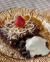A dessert plate with a brownie and a strawberry on top. The plate is made of gold and the dessert is served on a gold plate