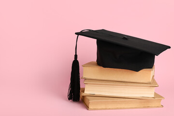 Mortar board with stack of books on pink background