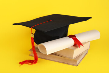 Mortar board with books and diploma on yellow background