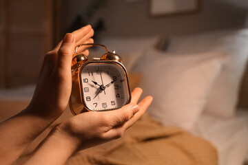 Female hands with alarm clock in bedroom at night, closeup