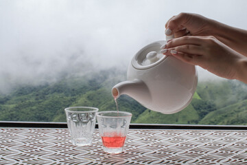Hand pouring tea from pot on table with fog on mountain at countryside homestay. Organic product from the nature for healthy.