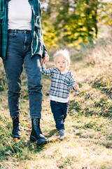 Little girl holding her mother hand walks along the green grass. Cropped