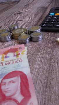 Nota adhesiva con la palabra pagos, con billete de 100 pesos mexicanos y monedas apilada, al fondo calculadora