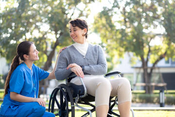 Young caucasian nurse comforting with patient while sitting on wheelchair in outdoor park, doctor...