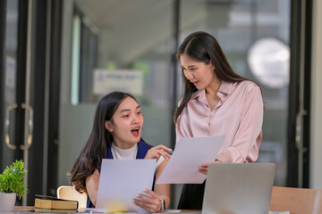 Two women are sitting at a desk with papers in front of them