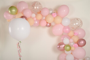 Garland of pink balloons placed on a white wall and a giant white helium balloon with flowers flying in the air for Mother's Day in a photo studio