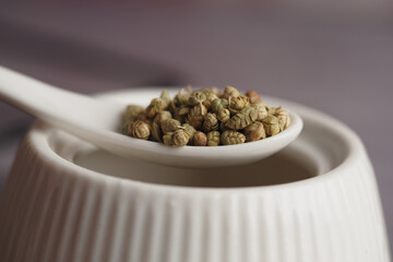 Dried herbal seeds in a white ceramic spoon on a kitchen table