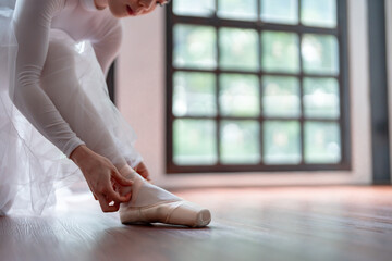 Ballerina in ballet shoes. Asian girl tying ribbons of toe shoes. ballet dancer preparing and wearing ballet shoes in dance studio prepares for a rehearsal.