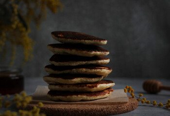 Pancakes in rows stacked close-up with honey and mimosa on a gray background