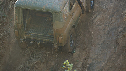 An off-road vehicle goes up a very steep slope. The vehicle is covered in mud and dust, demonstrating the difficult conditions in which it is traveling. Extreme racing.