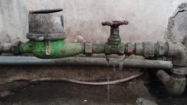 Water meter installation where its water flow opening and closing valve taps are damaged so that water appears to be dripping continuously around the tap.