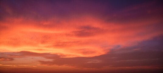 Peaceful evening sky in shades of red orange and violet with glowing clouds at sunset over quiet horizon, dreamy soft background for themes