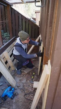 Man working on wooden wall repair outdoors during the old barn renovation. He uses hand tools and lumber to improve the structure. DIY, construction, and home maintenance.