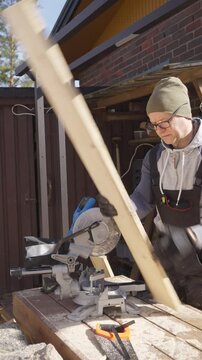 Man working outdoors on a carpentry project with a wooden boards and a circular saw, surrounded by tools and construction materials in a backyard workshop setting.