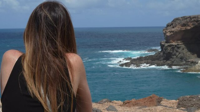 A woman with long dark hair admires the Atlantic Ocean from the coast. In the Ajui Caves on the island of Fuerteventura. Canary Islands, Spain.