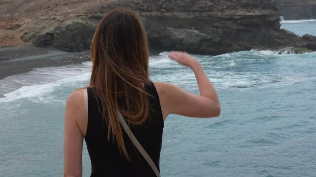 A woman with long, dark hair admires the Atlantic Ocean from the shore. On the island of Fuerteventura, Ajui Caves. Canary Islands, Spain.