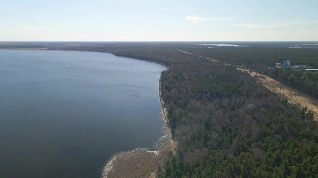 Aerial drone footage of &Uuml;lemiste lake water reservoir sandy shoreline, a large blue lake that is the water source fot surrounding Tallinn city. Electrical lines visible with horizon in the background.
