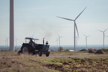 Farmers with tractors plowing the soil in a field full of windmills