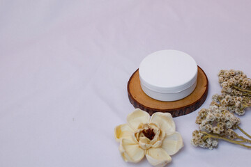 serene still life composition featuring a white cosmetic cream jar with a matching lid, elegantly placed on a natural wooden coaster.