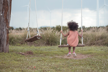 Little girl with swinging on a swing in picnic camping family day in wind turbine field