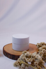 A minimalist and serene flat lay composition featuring a white, round cosmetic jar or container...
