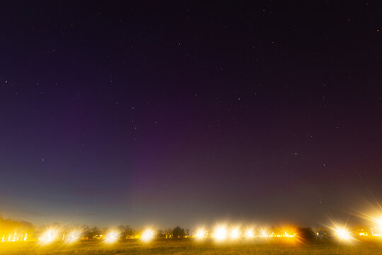 A starlit night sky fades into twilight above glowing city lights and a silhouette of trees on the horizon copy space in upper sky area.