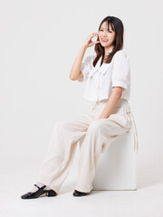 Asian young beautiful pretty happy woman she smiling, cute friendly wearing white shirt white pants sitting on white box pose isolated on white background studio portrait. Lifestyle fashion concept.