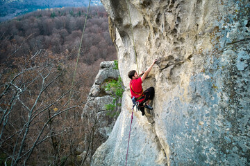 Aerial view of male rock climber ascending rugged limestone cliff with harness and rope for safety....