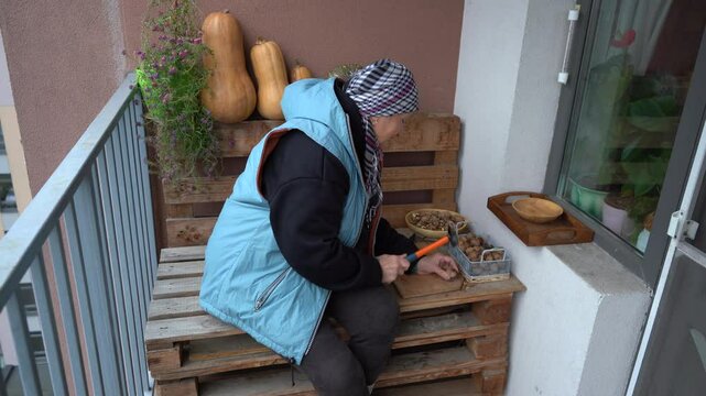Crack nuts with a hammer. An elderly woman peels a walnut. Grandmother cracking nutshell