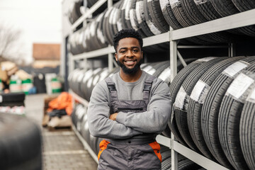 Portrait of multicultural mechanic standing with arms crossed near tires.