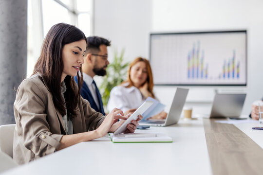 Side view of focused female employee scrolling on tablet and doing case study with her team.