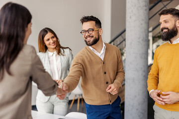Executive director shaking hands with new employee at corporate office in front of team of experts.
