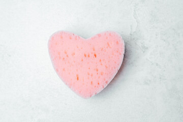 Fototapeta premium Cute heart-shaped sponge in light pink color on a textured surface
