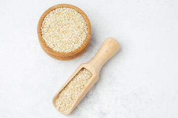 Sesame seeds in a wooden bowl and scooper on a light background