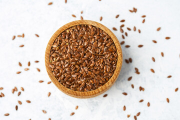 Brown flaxseeds in a wooden bowl on a light background