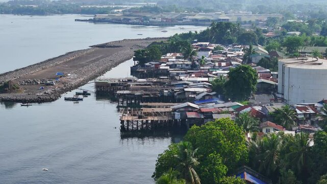 An aerial view captures rural coastal homes meeting industrial facilities along the Cagayan de Oro coastline in Mindanao, Philippines, highlighting the contrast between local life and industry.
