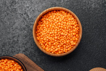 Bright orange lentils in a wooden bowl on a dark stone surface