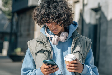 Teenage boy with headphones and mobile phone on the street eating a takeaway